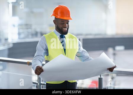 Worker Reads Construction Plans While Wearing a Hard Hat and Safety Vest in a Work Site Stock Photo