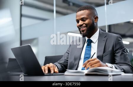 Businessman Works on Laptop in Office While Taking Notes During Meeting Hours for Company Tasks Stock Photo