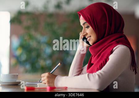 Side view of muslim woman talking on cellphone at cafe Stock Photo