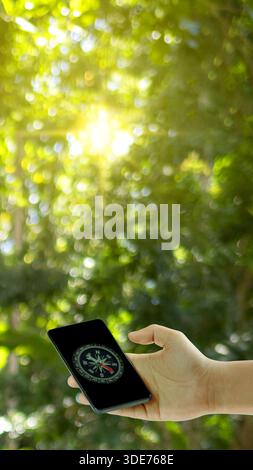 Person holding a smartphone with a compass app displayed on the screen, with a blurred natural green background. Concept of navigation, travel, explor Stock Photo