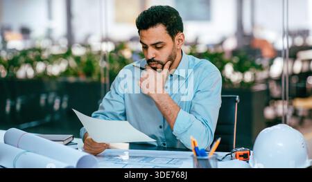 Man in Blue Shirt Studies Documents While Sitting in Modern Office Space Stock Photo