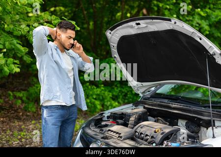 Sad arab man looking at engine and calling auto service Stock Photo