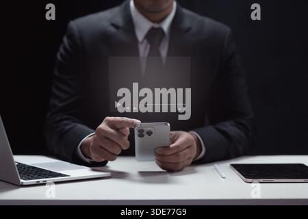 Businessman in a suit uses his smartphone to access a digital media interface with a play button and video controls. He's working at his desk with a l Stock Photo