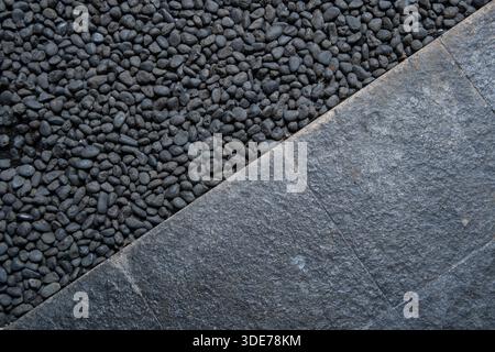 A top view of dark gray natural stone tiles and black river pebbles. A modern minimalist architectural textured backdrop for a garden or patio design. Stock Photo