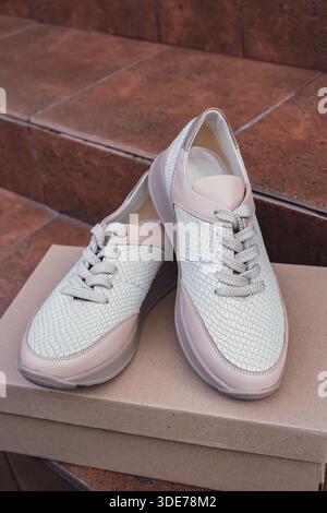 Minimalist eco-friendly white sneakers placed on recycled cardboard box, clean design for sustainable fashion concepts. New unbranded beige sneakers footwear mockups and modern product displays. For branding, e-commerce and packaging design Stock Photo