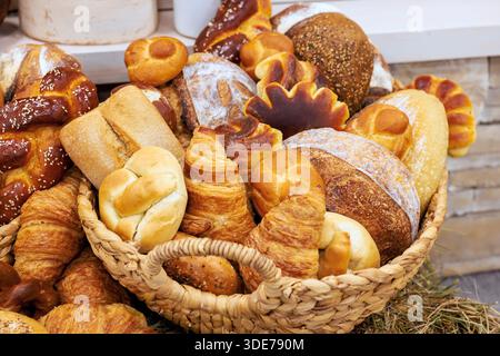 Woven basket filled with different types of freshly baked breads pastries arranged invitingly at local bakery Stock Photo