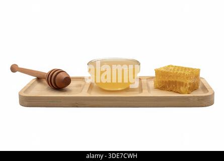 Glass bowl of honey with honeycomb and wooden dipper arranged on bamboo tray. Isolated composition showing natural sweet food and organic ingredients. Stock Photo