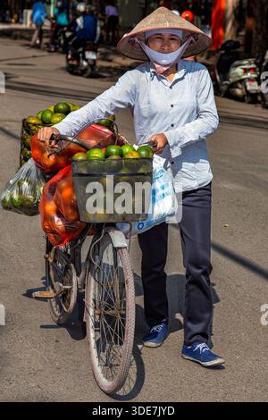 Vietnamese lady wearing bamboo hat, with bicycle, on street in Hanoi, Vietnam Stock Photo
