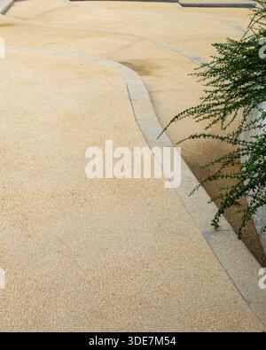Top down view of a yellow aggregate paved surface with curved lines and green plants on the side. The image conveys abstract texture and landscape pat Stock Photo