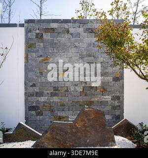 A textured grey stone wall design with rocks in a modern landscaped garden. The image conveys strength, stability, and contemporary design. High quali Stock Photo