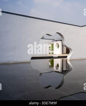 Angled view of a white architectural wall with a shaped cutout reflecting in dark, still water. The image conveys mystery, depth, and sophisticated la Stock Photo