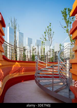 Vertical view of a spiral metal staircase or ramp adjacent to a layered orange wall and mirrored columns. The image conveys dynamic movement and archi Stock Photo
