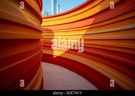 Close-up view of a modern architectural structure featuring layered orange curves illuminated by sunlight. The image conveys warmth, energy, and innov Stock Photo