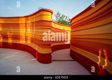 Scenic view of winding, wave-like architectural walls made of layered orange panels in an outdoor space. The image conveys rhythm, flow, and structura Stock Photo