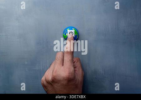 A finger pressing a power button on a miniature globe. Earth Hour, energy saving, energy conservation concept. Stock Photo