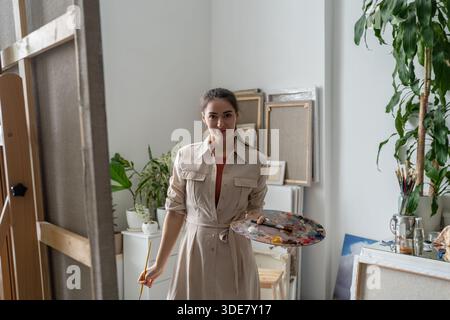 Confident cheerful female artist painting picture at creative home workshop, art hobby therapy. Stock Photo