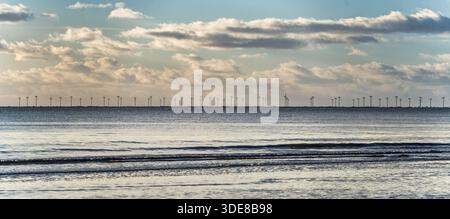 A peaceful coastal scene featuring calm water, gentle waves, and distant wind turbines on the horizon. Soft clouds drift above, evoking sustainable en Stock Photo