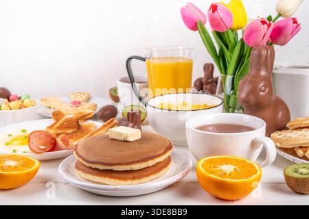 Easter holiday sweet breakfast, brunch. Easter decorated belgian waffles, pancakes, breakfast cereals and milk, fried eggs with toasts and bacon, East Stock Photo
