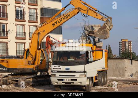 A yellow Hyundai hydraulic excavator loading concrete debris and rubble into a dump truck during a residential demolition Stock Photo