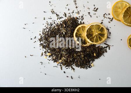 Detail of a pile of dried tea leaves isolated on a white table with lemon slices. Top view. Stock Photo