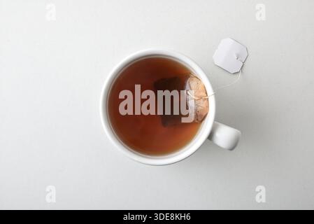 Detail of infusion in a white ceramic cup with herbs in a sachet inside the cup isolated in the center of a white table. Top view. Stock Photo