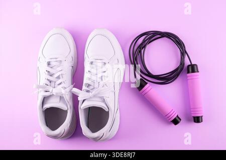 Fitness accessories concept. Top view photo of white sneakers and skipping, jump rope on isolated pink background. Flatlay Stock Photo