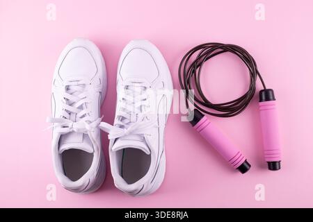 Fitness accessories concept. Top view photo of white sneakers and skipping, jump rope on isolated pink background. Flatlay Stock Photo