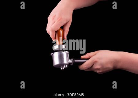 Man is using a tamper to press freshly ground morning coffee into a coffee tablet on isolated black background Stock Photo