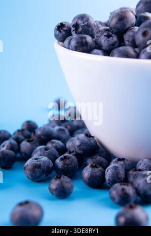 Blueberries on a macro scale. Dark berries in bowl close-up. Ripe blueberries isolated on blue background. Healthy, natural fruit. Stock Photo