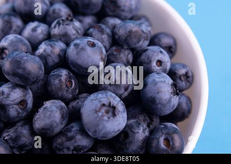 Blueberries on a macro scale. Dark berries in bowl close-up. Ripe blueberries isolated on blue background. Healthy, natural fruit. Stock Photo