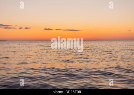A picturesque colorful dawn is reflected in water of Baikal Lake in early spring morning. A seagull sways on waves of Small Sea. Beautiful seascape. N Stock Photo