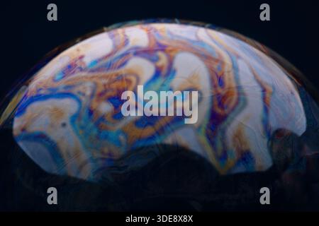 Vivid abstract patterns on the surface of a soap bubble with swirling colors and dark background, ideal for creative and scientific concepts. Stock Photo
