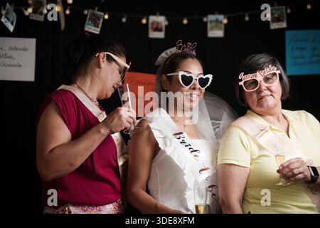 A woman in a white dress with a bride's veil is standing in front of a black background. Two other women are standing behind her. One of the women is Stock Photo
