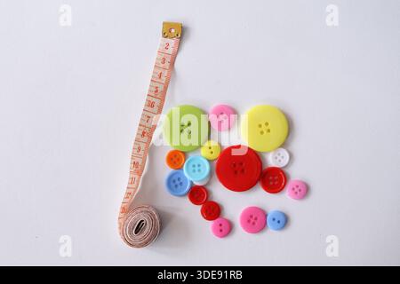 Top view of various colorful buttons next to a curled tailor measuring tape on a white surface. Creative sewing and craft concept. Stock Photo