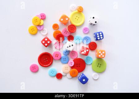 Top view of various colorful sewing buttons and gaming dice scattered on a white surface. Creative hobby and play concept. Stock Photo