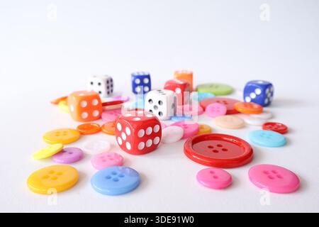 Top view of various colorful sewing buttons and gaming dice scattered on a white surface. Creative hobby and play concept. Stock Photo