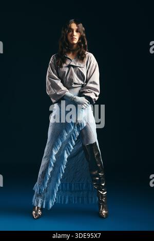 Young woman stands confidently in a chic, attention-grabbing outfit against a striking background. Stock Photo