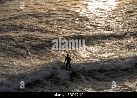 Estoril Portugal December 17 2025. A surfer rides a breaking Atlantic wave during sunset with golden light reflecting on the water Stock Photo