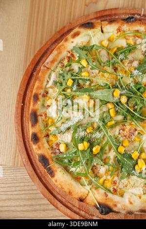 A selection of food items from various cuisines is displayed on a wooden table. Dishes include pizza topped with corn and greens. Fresh ingredients ar Stock Photo