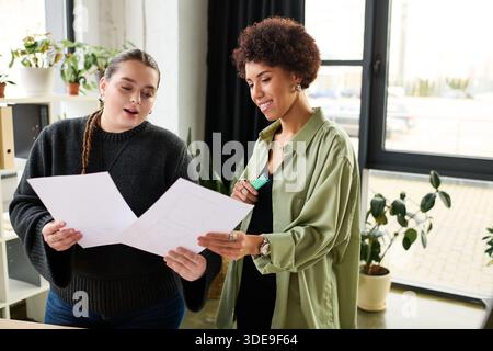Two female managers discuss plans while reviewing documents in a bright, stylish workspace. Stock Photo