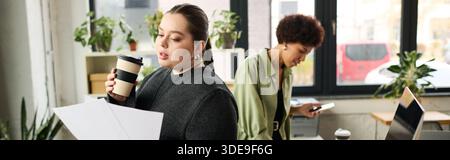 In a modern office, a young plus size woman reviews documents while her colleague works nearby, banner Stock Photo