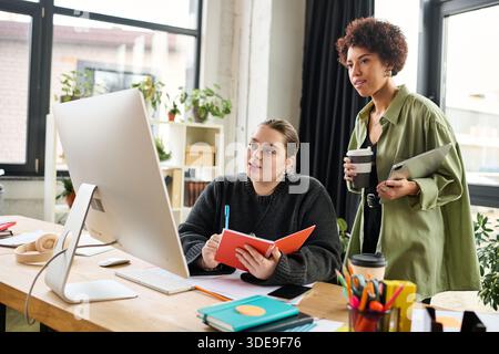 Two women share ideas in a modern workspace, fostering creativity and teamwork. Stock Photo