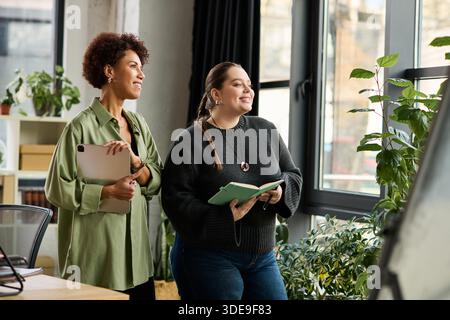 Two female managers share ideas and smiles while working in a vibrant office environment. Stock Photo