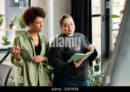 Two young professional women share ideas while working together in a stylish corporate environment. Stock Photo