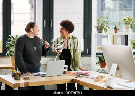 Two female managers share ideas and laughter while collaborating in a bright office. Stock Photo