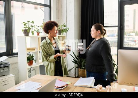 Two female managers have a lively discussion while holding coffee cups in a bright office. Stock Photo