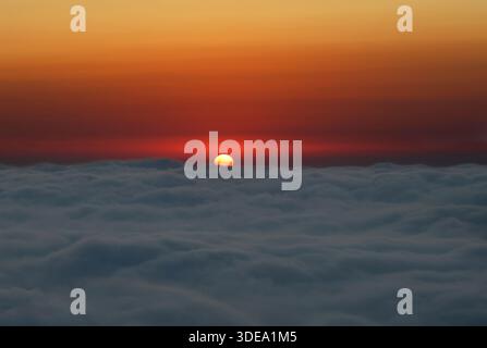 Sun setting behind soft clouds viewed at eye level, creating a calm and atmospheric sky scene. Stock Photo