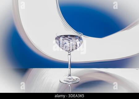 Close up view of elegant cocktail glass with ice cubes on abstract blue and white background. Stock Photo