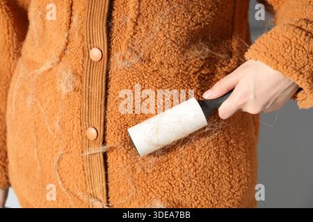 Woman cleaning cardigan with lint roller on light grey background, closeup Stock Photo
