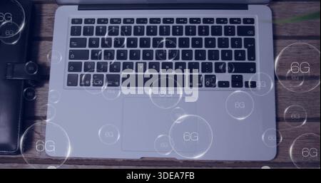 Showing silver laptop displaying keyboard, trackpad on wood table with black folio and 6G overlays Stock Photo